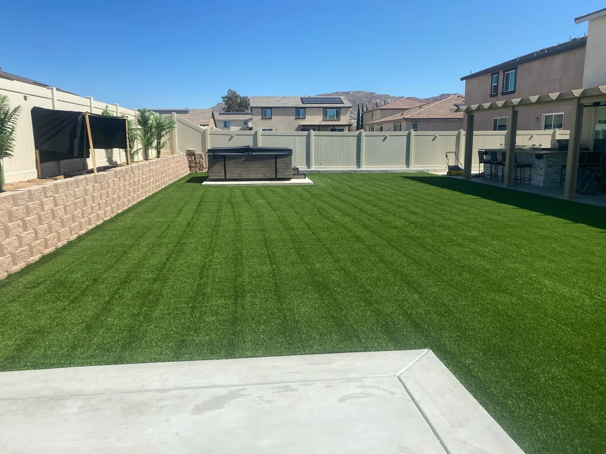 Artificial turf backyard beside a raised planter, hot tub, and covered patio