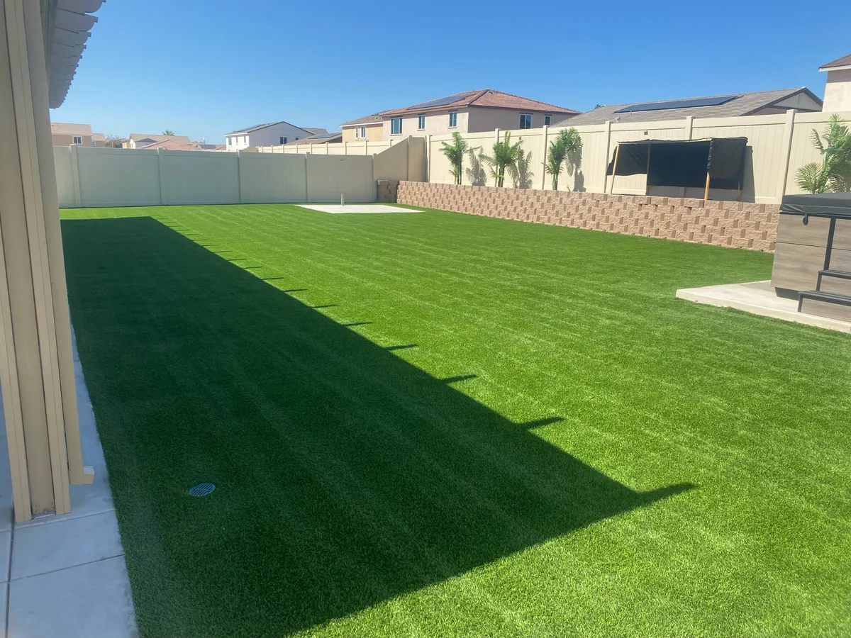 Wide artificial turf lawn with grooming lines, a raised planter, and white fencing