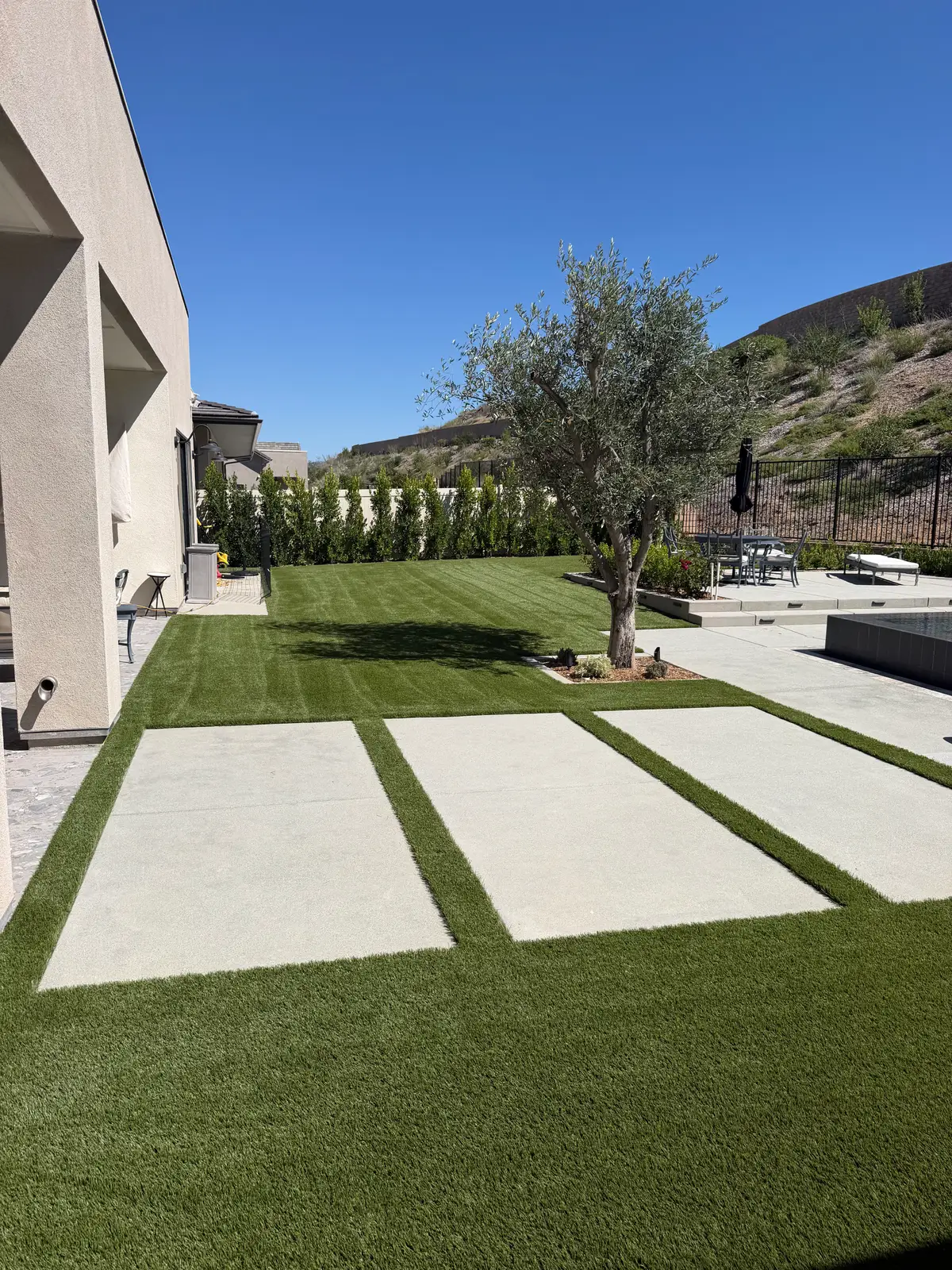 Artificial turf surrounding concrete stepping slabs beside a poolside patio
