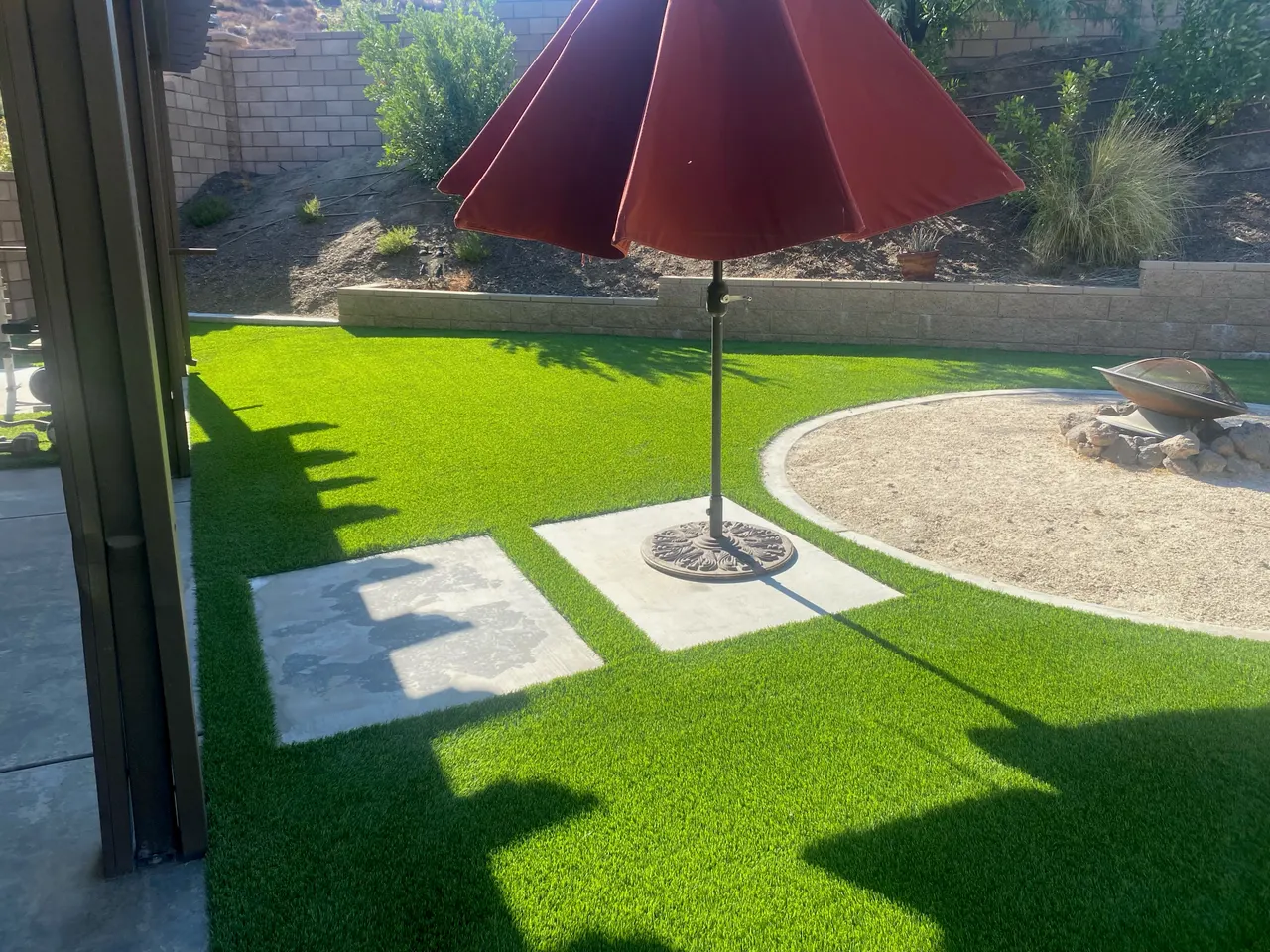 Artificial turf surrounding concrete stepping slabs, a patio umbrella, and a fire pit in Folsom