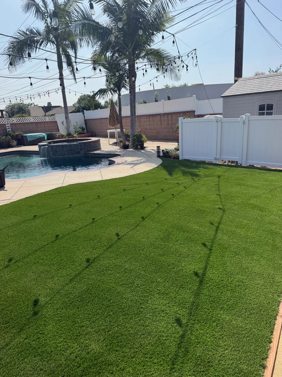 Artificial turf beside a backyard pool and spa with palm trees and string lights in Newport Beach